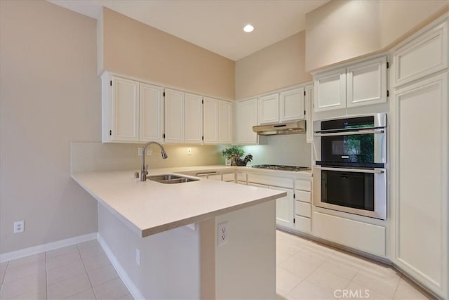 kitchen with light countertops, stainless steel double oven, a sink, a peninsula, and under cabinet range hood