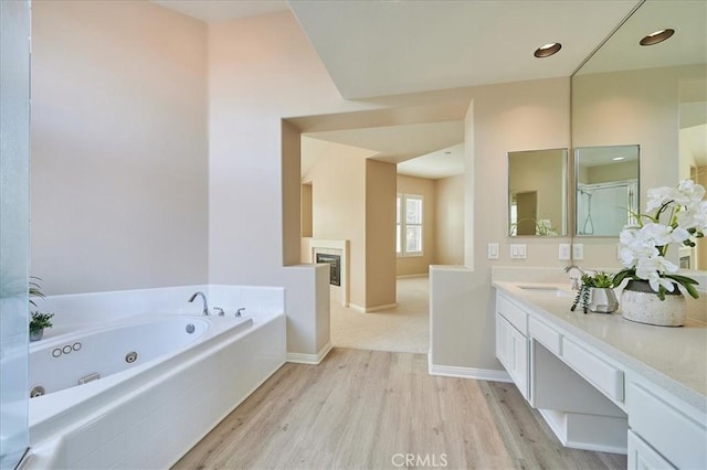 bathroom with baseboards, wood finished floors, a whirlpool tub, vanity, and a fireplace