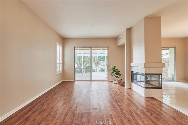 unfurnished living room with a tile fireplace, visible vents, baseboards, and wood finished floors