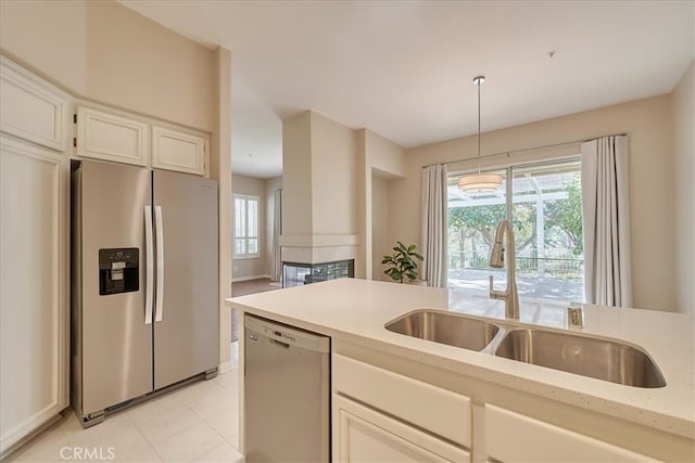 kitchen with light tile patterned flooring, stainless steel appliances, a sink, white cabinets, and pendant lighting