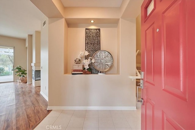 entryway with visible vents, a fireplace, baseboards, and light tile patterned flooring