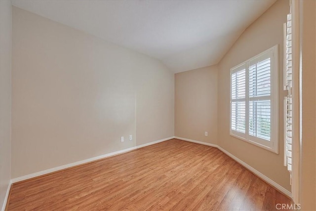 unfurnished room featuring vaulted ceiling, light wood finished floors, and baseboards