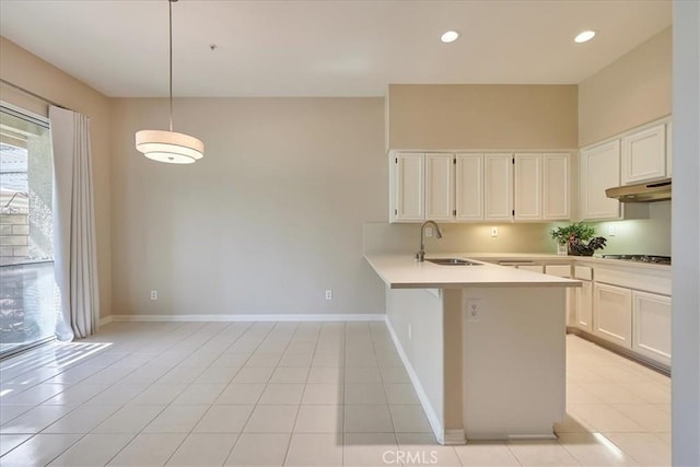 kitchen featuring light countertops, white cabinetry, a sink, a peninsula, and under cabinet range hood