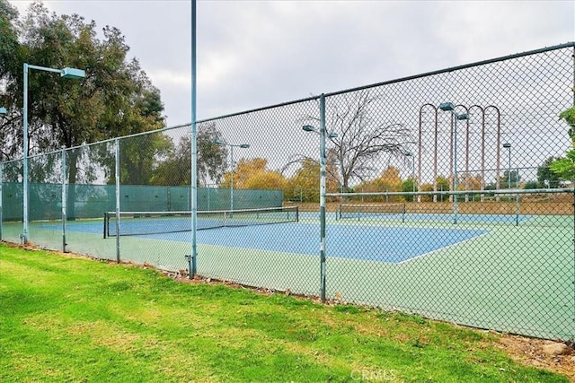 view of tennis court featuring fence and a lawn