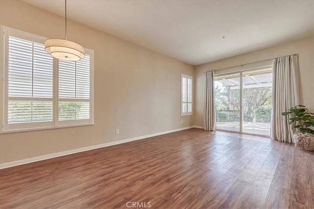 empty room featuring plenty of natural light, wood finished floors, and baseboards