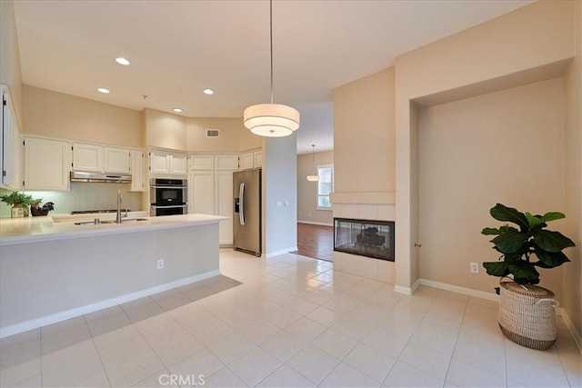 kitchen with a tile fireplace, appliances with stainless steel finishes, a peninsula, light countertops, and under cabinet range hood