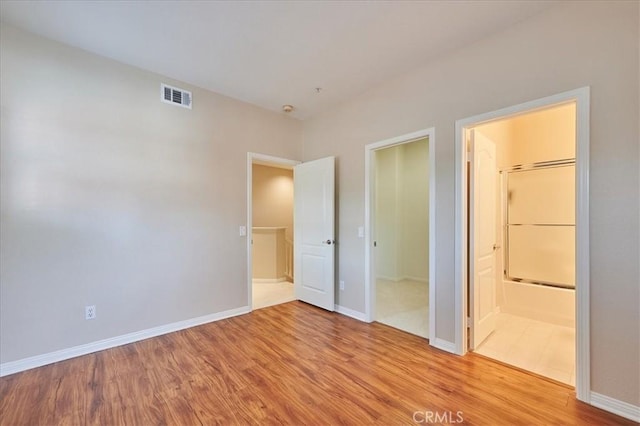 unfurnished bedroom featuring ensuite bath, baseboards, visible vents, and wood finished floors