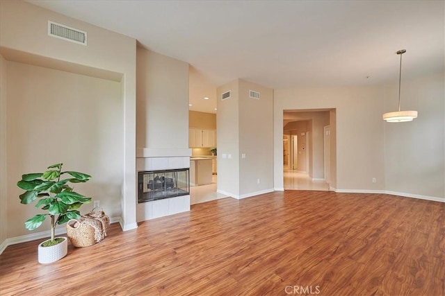 unfurnished living room with light wood finished floors, visible vents, and a tile fireplace