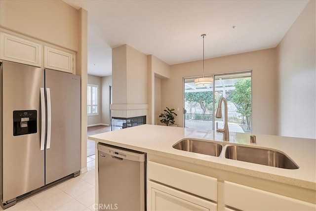 kitchen with appliances with stainless steel finishes, decorative light fixtures, white cabinetry, a sink, and light tile patterned flooring