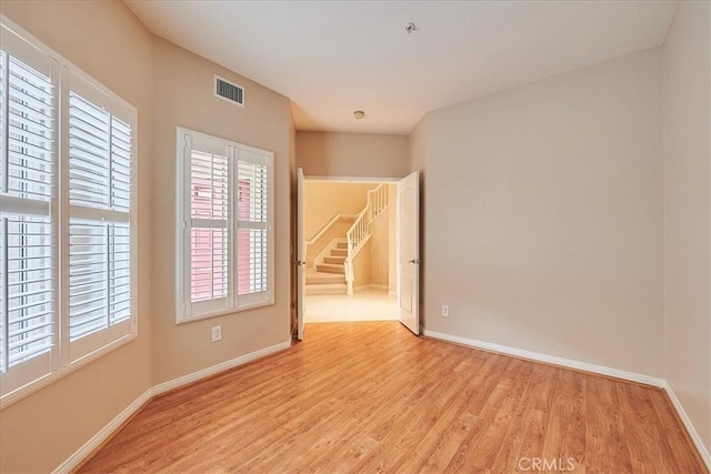 unfurnished room featuring stairway, visible vents, light wood-style flooring, and baseboards