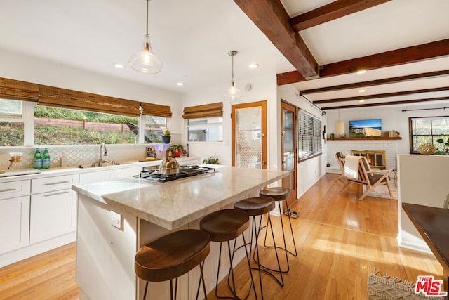 kitchen with white cabinetry, a kitchen island, pendant lighting, beam ceiling, and light stone counters