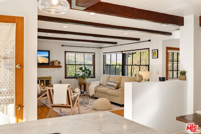 living room with a brick fireplace, light hardwood / wood-style flooring, and beamed ceiling