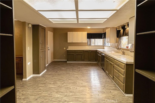 kitchen featuring light wood finished floors, light countertops, stainless steel dishwasher, a sink, and baseboards