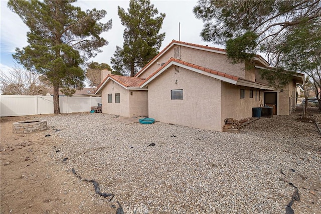 rear view of house with an outdoor fire pit, fence, a tiled roof, and stucco siding