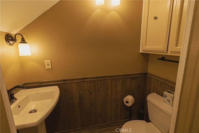 bathroom with sink, wooden walls, and toilet