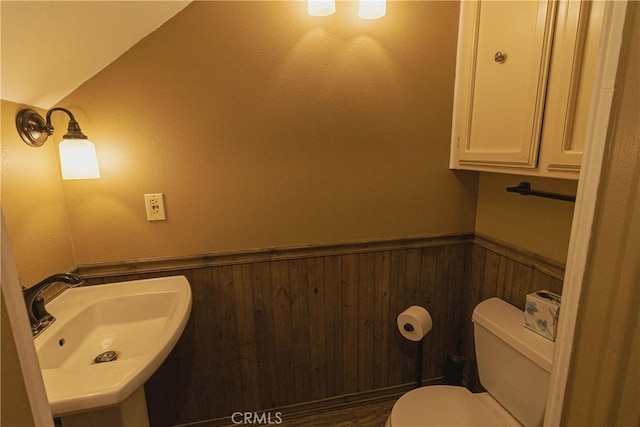 bathroom with toilet, wood walls, a sink, and wainscoting