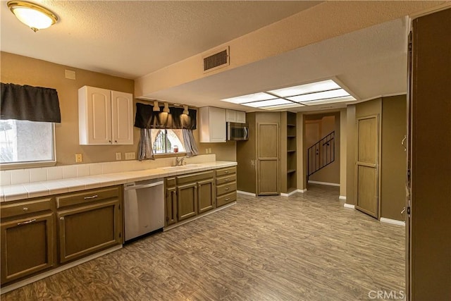 kitchen featuring sink, stainless steel appliances, a textured ceiling, tile countertops, and light wood-type flooring