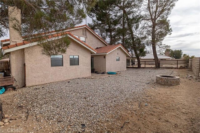 back of property with fence private yard, a tile roof, a fire pit, and stucco siding