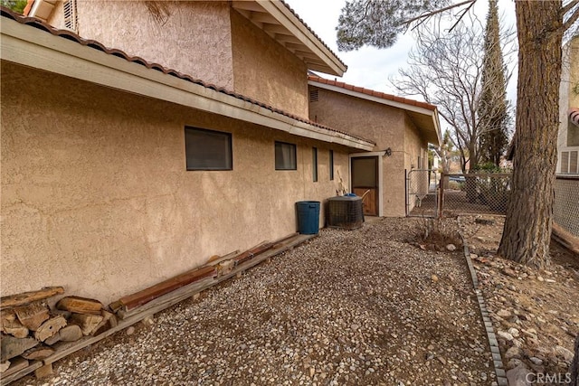 view of side of property with fence, a tiled roof, central AC unit, and stucco siding