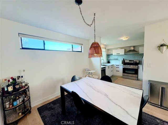 kitchen with decorative backsplash, decorative light fixtures, wall chimney range hood, stainless steel range oven, and white cabinets