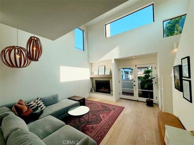 living room with french doors, a towering ceiling, a notable chandelier, and light hardwood / wood-style floors