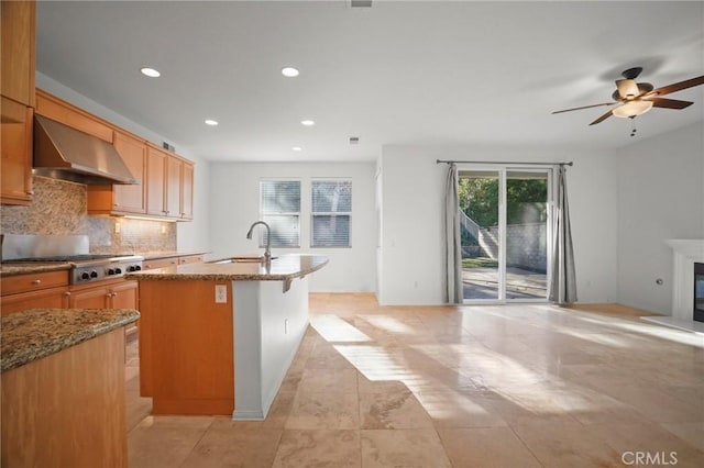 kitchen featuring wall chimney exhaust hood, a breakfast bar, sink, a center island with sink, and stainless steel gas stovetop