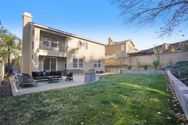 back of property with a balcony, an outdoor hangout area, a patio, and a lawn