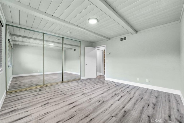 unfurnished bedroom with beamed ceiling, light hardwood / wood-style floors, and a closet