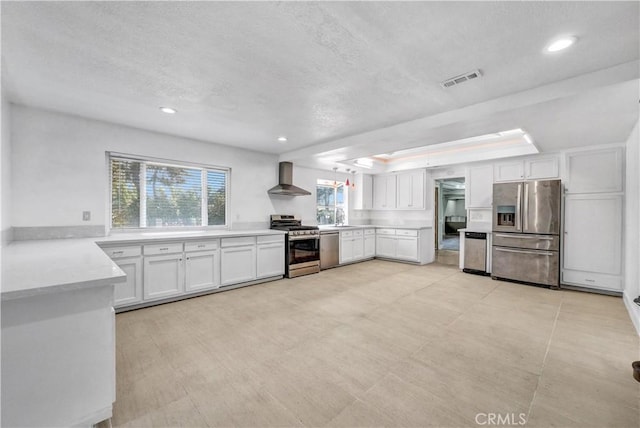 kitchen featuring wall chimney exhaust hood, stainless steel appliances, a tray ceiling, sink, and white cabinetry