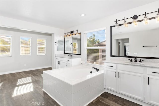 bathroom with hardwood / wood-style flooring, tiled tub, and vanity