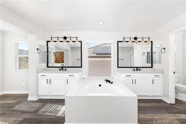 bathroom with toilet, vanity, tiled bath, and hardwood / wood-style flooring