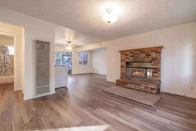 unfurnished living room featuring a textured ceiling, ceiling fan, a fireplace, and wood-type flooring