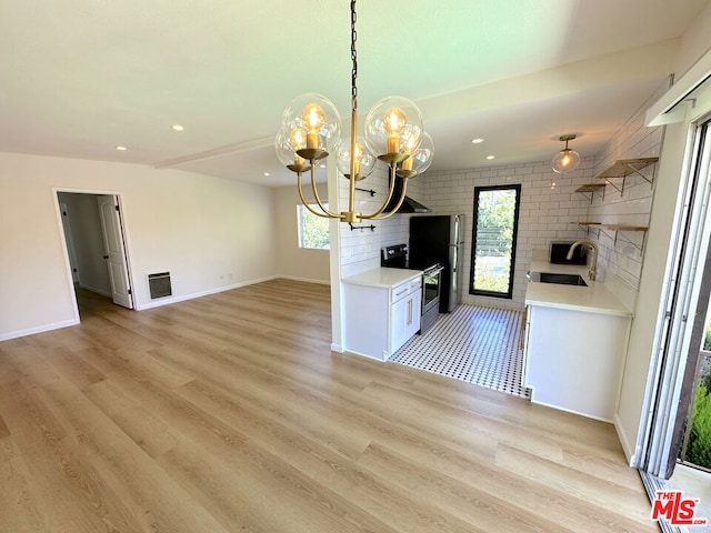 kitchen with white cabinets, stainless steel range with electric cooktop, an inviting chandelier, sink, and hanging light fixtures