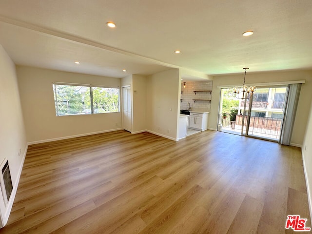 unfurnished living room featuring light wood-type flooring, a notable chandelier, and plenty of natural light