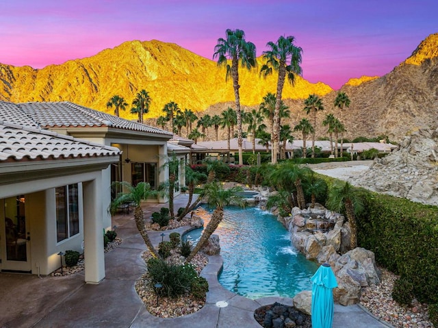 pool at dusk featuring pool water feature, a patio area, and a mountain view