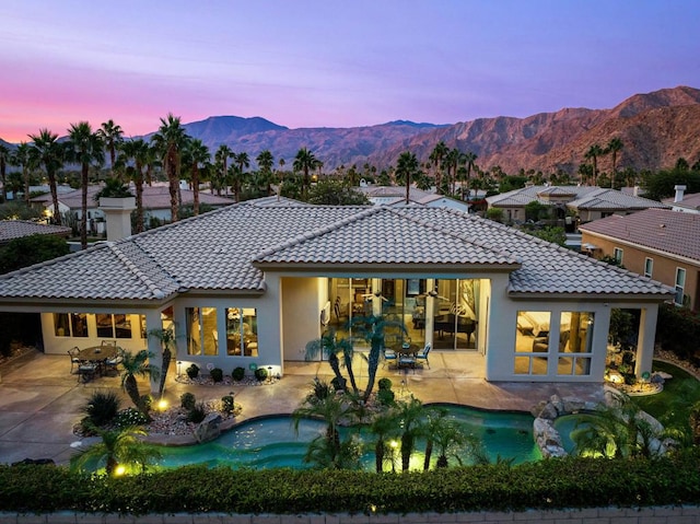 back house at dusk featuring a mountain view and a patio area