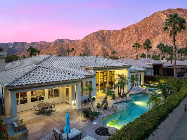 back house at dusk featuring a mountain view and a patio