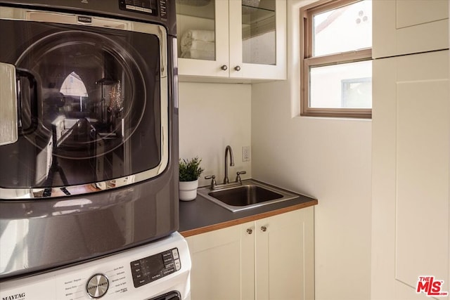 clothes washing area with cabinets, stacked washer / drying machine, and sink