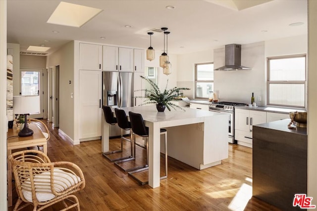 kitchen featuring pendant lighting, a center island, wall chimney exhaust hood, white cabinetry, and stainless steel appliances