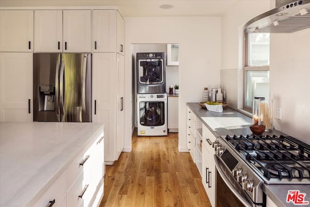 kitchen featuring range hood, light hardwood / wood-style floors, stacked washer / dryer, stainless steel appliances, and white cabinets