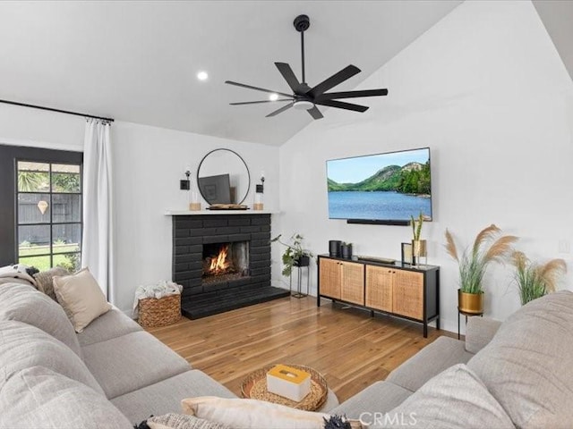 living room with a brick fireplace, wood-type flooring, lofted ceiling, and ceiling fan