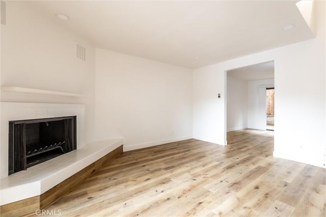 unfurnished living room with a tiled fireplace and light hardwood / wood-style flooring