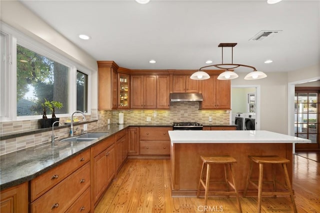 kitchen featuring washer and dryer, gas stove, decorative backsplash, sink, and hanging light fixtures