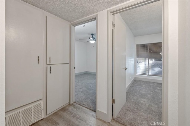 hall with light carpet and a textured ceiling