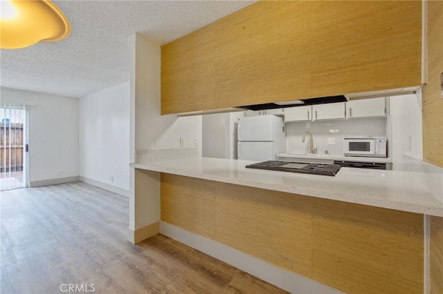 kitchen featuring white appliances, a textured ceiling, kitchen peninsula, and white cabinets