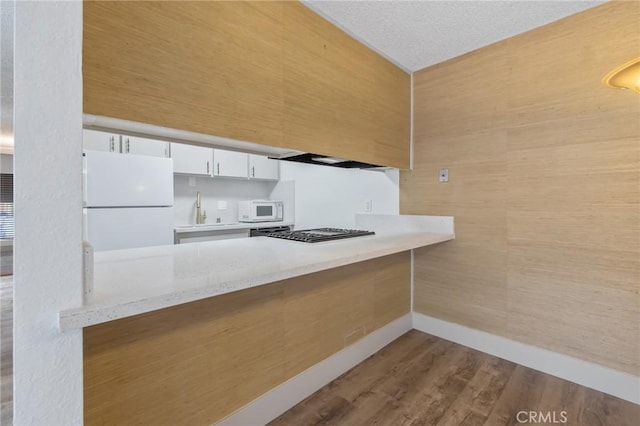 kitchen with sink, white cabinetry, kitchen peninsula, white appliances, and light hardwood / wood-style floors