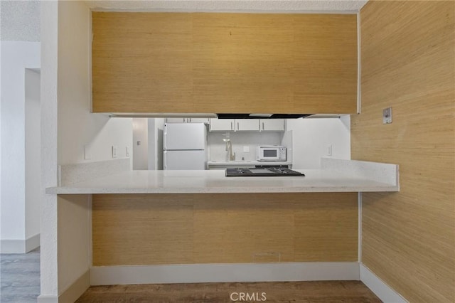 kitchen with light wood-type flooring, wooden walls, kitchen peninsula, white appliances, and white cabinets