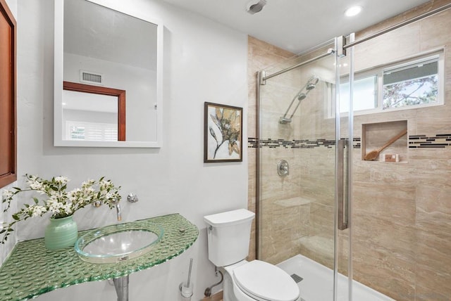 bathroom featuring toilet, a shower with door, and sink