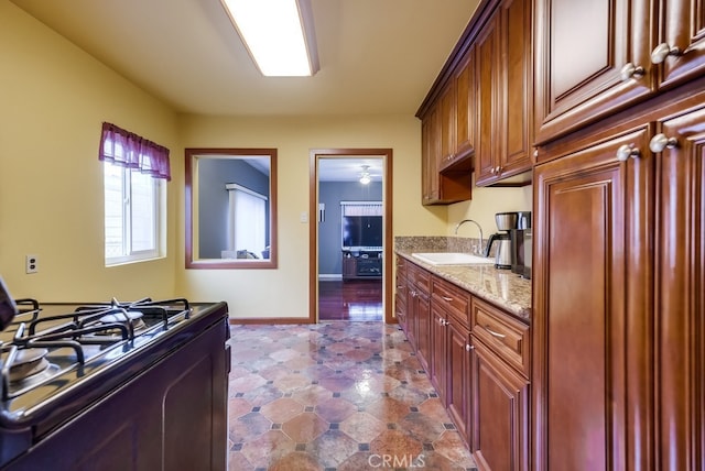 kitchen featuring light stone counters, sink, and range with gas stovetop