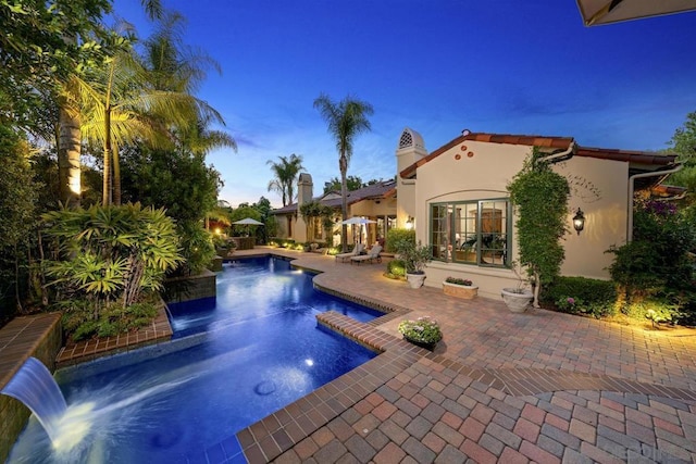 pool at dusk featuring pool water feature and a patio